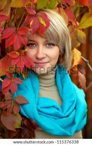 Autumn portrait a lovely young gray-eyed blond woman. A beautiful face is framed by bright colorful autumn leaves.
