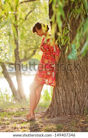 A lonely woman standing near the tree by the river