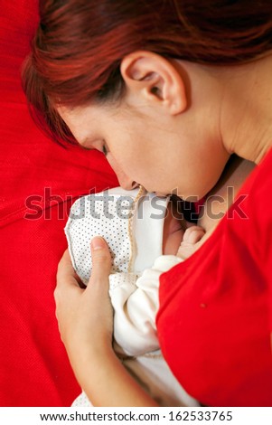 Happy mother and her newborn baby sleeping in bed. Mom kissing baby\'s head. Concept of love, care, happiness and pacification