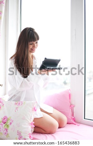 Young woman checking email and social networking accounts using tablet PC early in the morning, waking up recently. Modern technology and network concept.