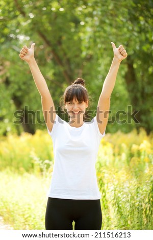 Woman in white t-shirt showing a thumbs up sign outdoors. Ready for your logotype, text or symbols.