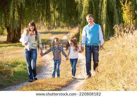 Big happy family walking along the path in the park. Father, mother, son, daughter and baby holding hands and going together. Family Ties concept.