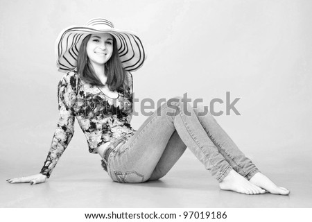 Black and white portrait. Young beautiful  long haired woman wearing a hat and jeans, sitting on the floor. Vintage style