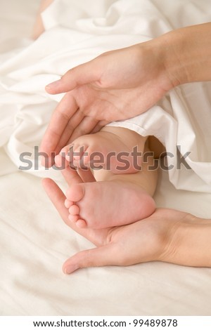Baby feet in mother\'s hands, heart-shaped. The symbol of protection, custody and parental love