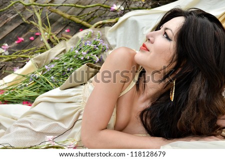 Young beautiful woman lie down with flowers outdoor and looking into the distance