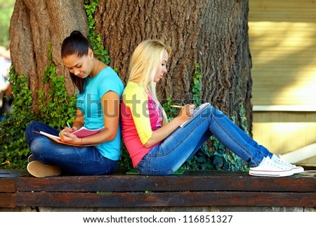 two beautiful young girls getting knowledge on bench under an old oak tree