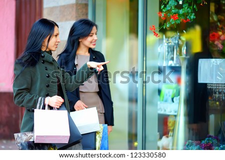happy girls with shopping bags pointing finger in the shop window