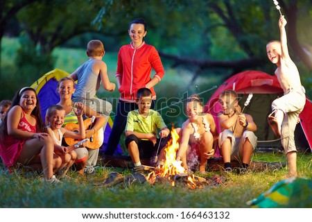 group of happy kids roasting marshmallows on camp fire