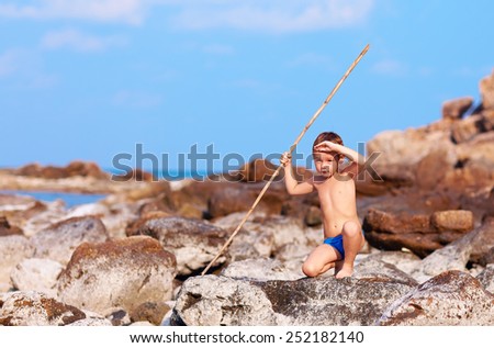 cute boy with bamboo spear pretends like he is aborigine on desert island