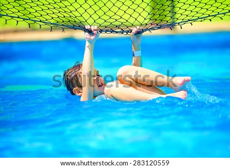 cute boy kid having fun, making stunt on volleyball net in pool