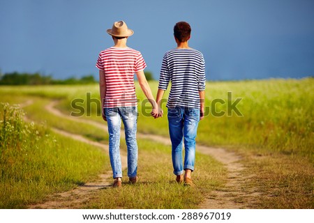 young male couple walking away on summer field path