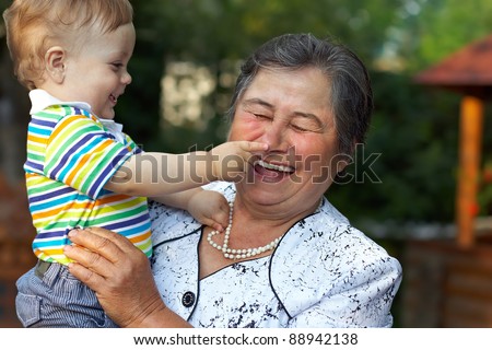 cute grandson grabbing the nose of laughing great grandmother. funny outdoors