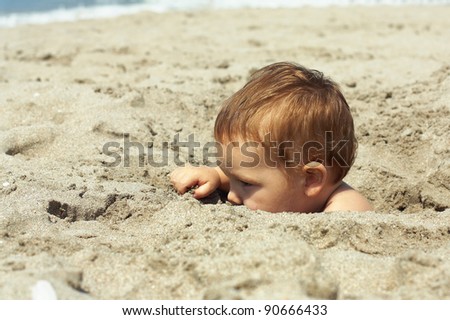little baby boy hiding himself in sand on the beach. only head is visible