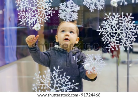 curious little baby boy looking at snowflakes on shop window in city mall