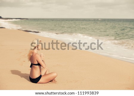 Beautiful Blonde sitting in the Quiet of the Beach in prayer pose