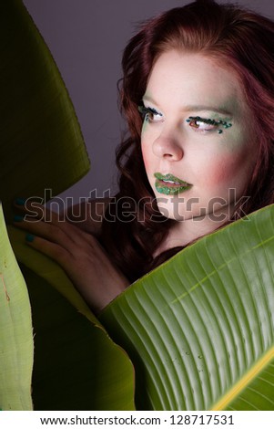 Beautiful red headed woman looking from behind a Bird of paradise