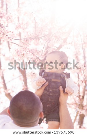 Father lifting his son into the sun for a sun flared  softened portrait of a Happy Baby