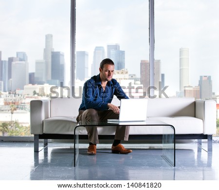 Attractive casual business man working in a Penthouse Suite with Los Angeles Skyline behind him