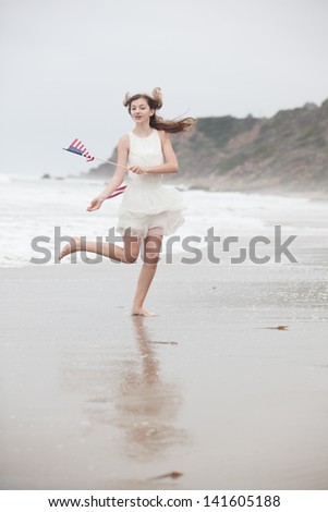 Beautiful Teen Girl having fun with American flags on the beach