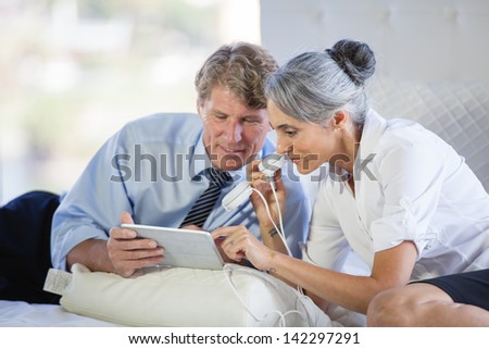 Attractive Mature couple listening to music on Headsets from a Mini touch Pad on a bed after work