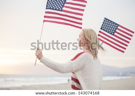 Pretty Young Woman at the Beach holding American Flags facing the ocean