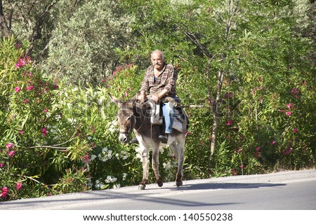 GREECE, CRETE - MAY 27. Old man riding a donkey on the street on Crete on may 27, 2013. In the mountains on Crete the donkey is still used as a means of transportation. An old Greek tradition