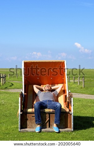 Relaxed man enjoys on a roofed wicker beach chair on the Hallig Langeness