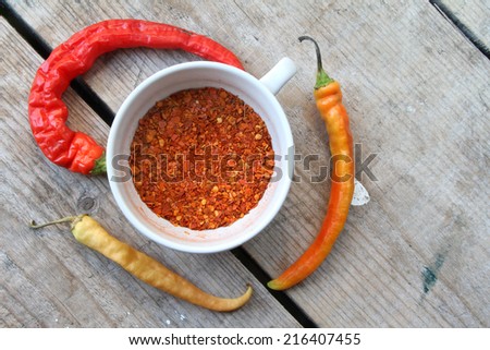 ground cayenne pepper  in white bowl and fresh red hot chili peppers on wooden surface