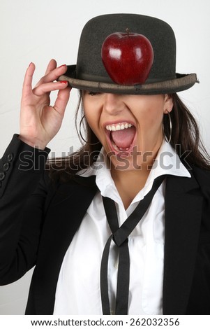 The girl and apple - Beautiful young brunette with red nail polish, bowler hat on head in a white shirt with a black tie, black jacket holding a red fresh apples on a hat with funny facial expressions