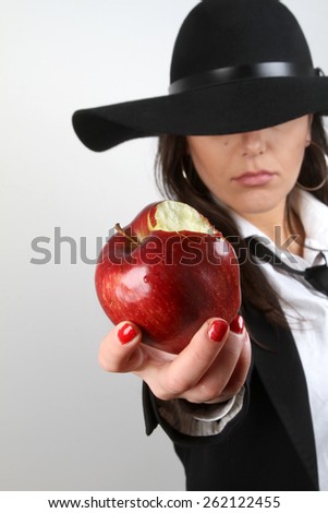 Apple and a girl - beautiful young brunette smiling holding fresh organic healthy bitten apple in the palm of her hand with a hat on his head in a black jacket and white shirt