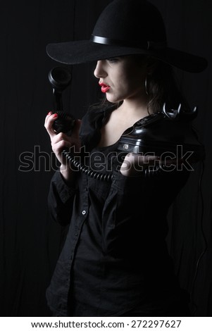 beautiful young brunette woman lady posing in a studio on a black background with old style hat  holding a telephone