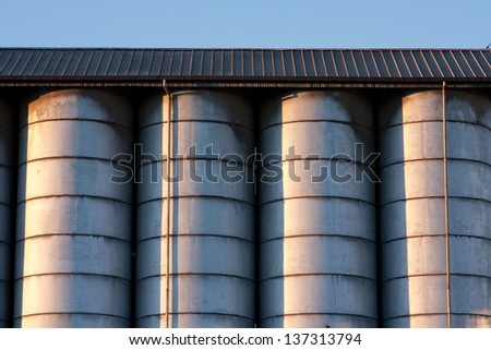 Line of metal silos under a roof with radent sunlight with contrast and light reflex
