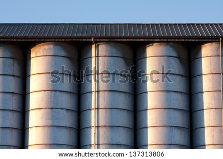 line of metal silos under a roof with radent sunlight with contrast and light reflex