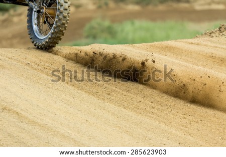 Motocross machine wheel and raised dust captured right after the motocross race machine starts off, no recognizable people