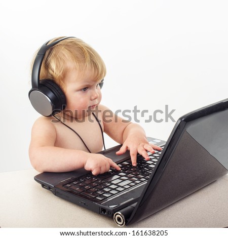 Cute little girl is sitting at table with her black laptop, isolated over white