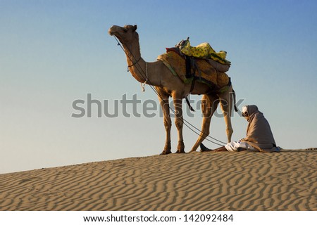 JAISALMER, INDIA-FEB 26: Cameleer waits for tourists at Sam Sand Dune on Feb 26, 2013 in Jaisalmer, India. Apart from farming, camel riding activity is another income source for desert villagers
