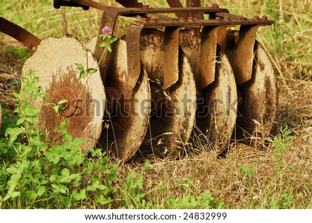 Vintage farm equipment, harrow, with five steel discs covered with clay and rust.