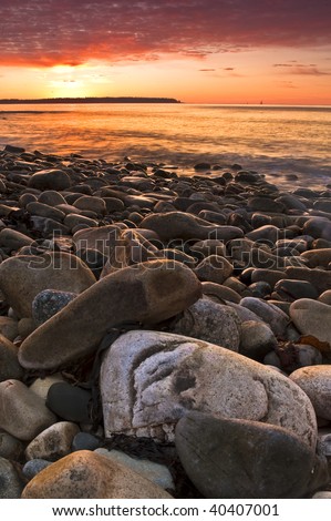 A face on a rock in the foreground is smiling as the sunrises over the ocean.