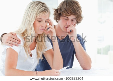 A worried couple hold each other as they look at a pregnancy test