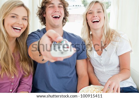 Laughing friends with a bowl of popcorn as they use the tv remote