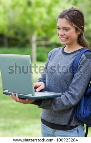 Young student looking at the screen of her laptop while smiling and standing upright