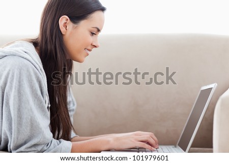 A smiling woman lying on the couch as she types on her laptop