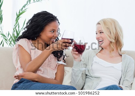 Two women sitting on a couch are holding wine glasses and smiling at each other