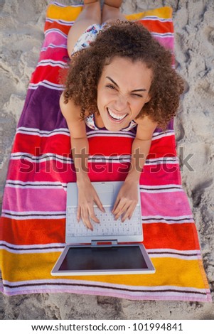 Young smiling woman looking at the camera while using her laptop on the beach
