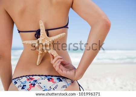 Young woman standing on the beach holding a starfish on her back with one hand