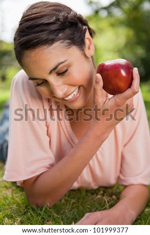 Woman looking down towards the ground while presenting a red apple as she is lying down in grass