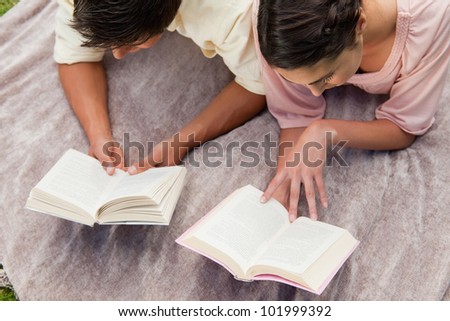 Elevated view of a man and a woman reading books while lying prone on a blanket in the grass