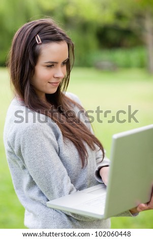 Young relaxed woman holding her laptop while standing upright in the countryside
