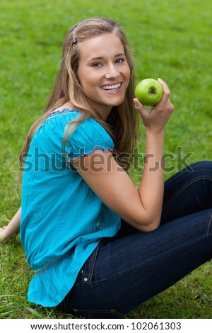 Smiling young woman holding a delicious apple while sitting down in the countryside