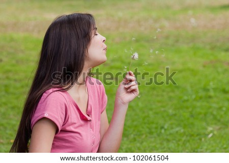 Young relaxed woman blowing a dandelion while standing in the countryside